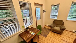 Una habitación con piso de madera, una silla verde, un sillón marrón y una mesa con una planta.