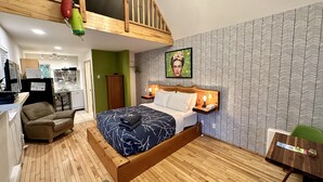 Un dormitorio con cama estilo loft, una pared verde, papel tapiz estampado, cabecera de madera y una mesita de noche pequeña con lámpara.