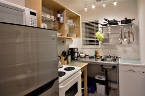 Cocina compacta con refrigerador, estufa, lavavajillas y repisas de madera con utensilios de cocina.