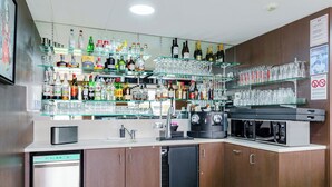 A bar area with shelves of liquor bottles and glasses, a coffee machine, and a microwave. - roi soleil prestige (Saint-Avold)