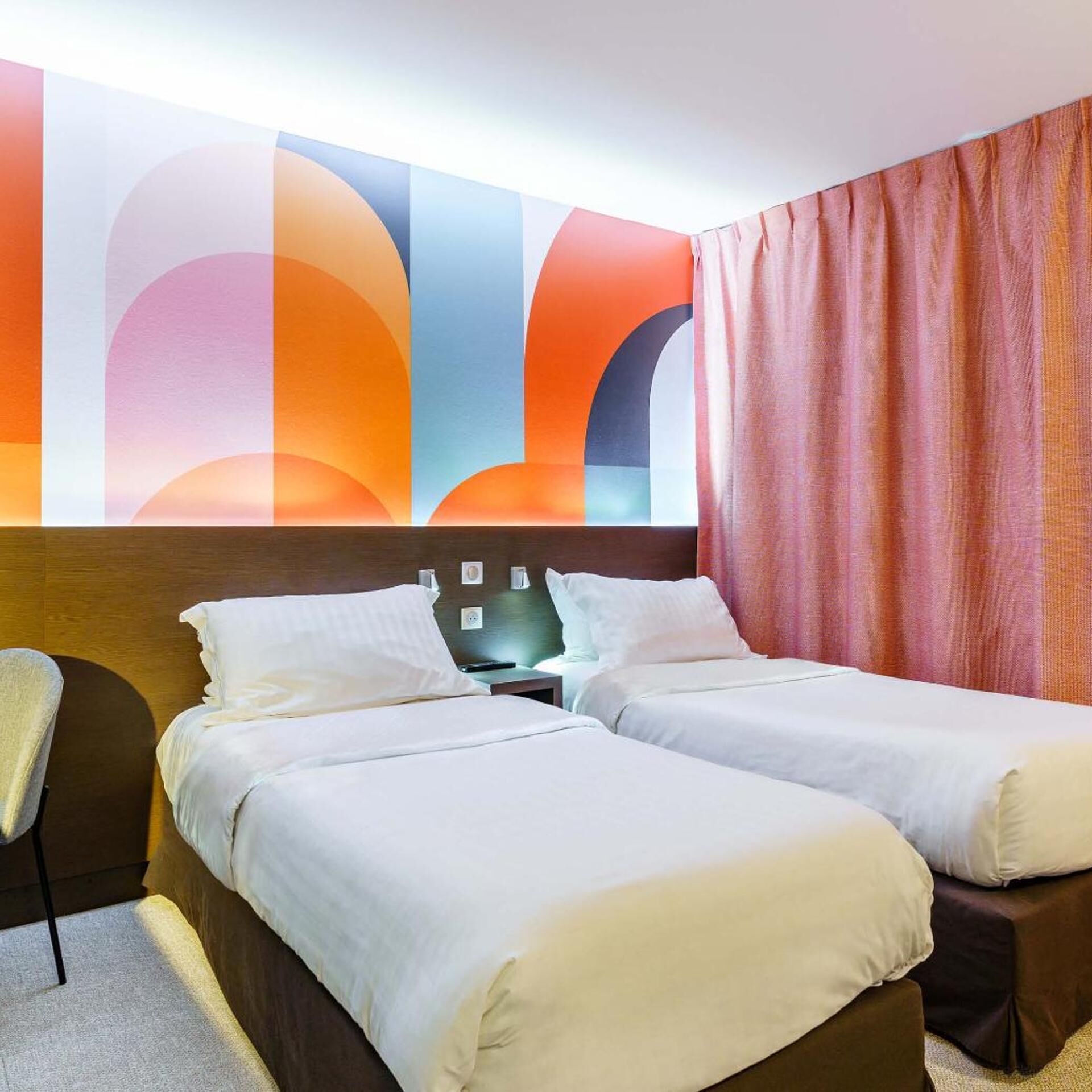 Een hotelkamer met twee bedden, een houten hoofdeinde, een nachtkastje en een groot abstract wanddecor.