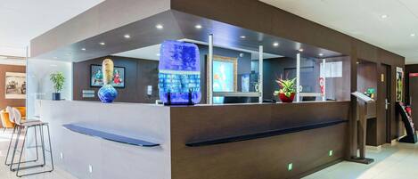 A modern reception desk with a glass partition, a blue decorative piece, and a seating area with chairs.