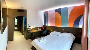 A hotel room with a bed, a desk, and a bathroom visible through an archway. - roi soleil prestige (Saint-Avold)