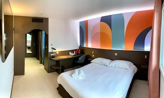A hotel room with a bed, a desk, and a bathroom visible through an archway.