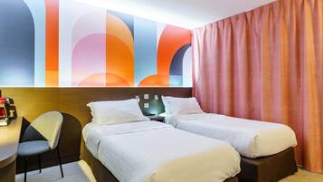 Une chambre d’hôtel avec deux lits, un bureau, une chaise et une fresque murale abstraite et colorée.