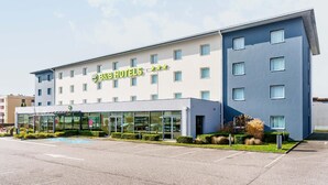 A B&B hotel with a modern facade, large windows, and a parking lot. - roi soleil prestige (Saint-Avold)