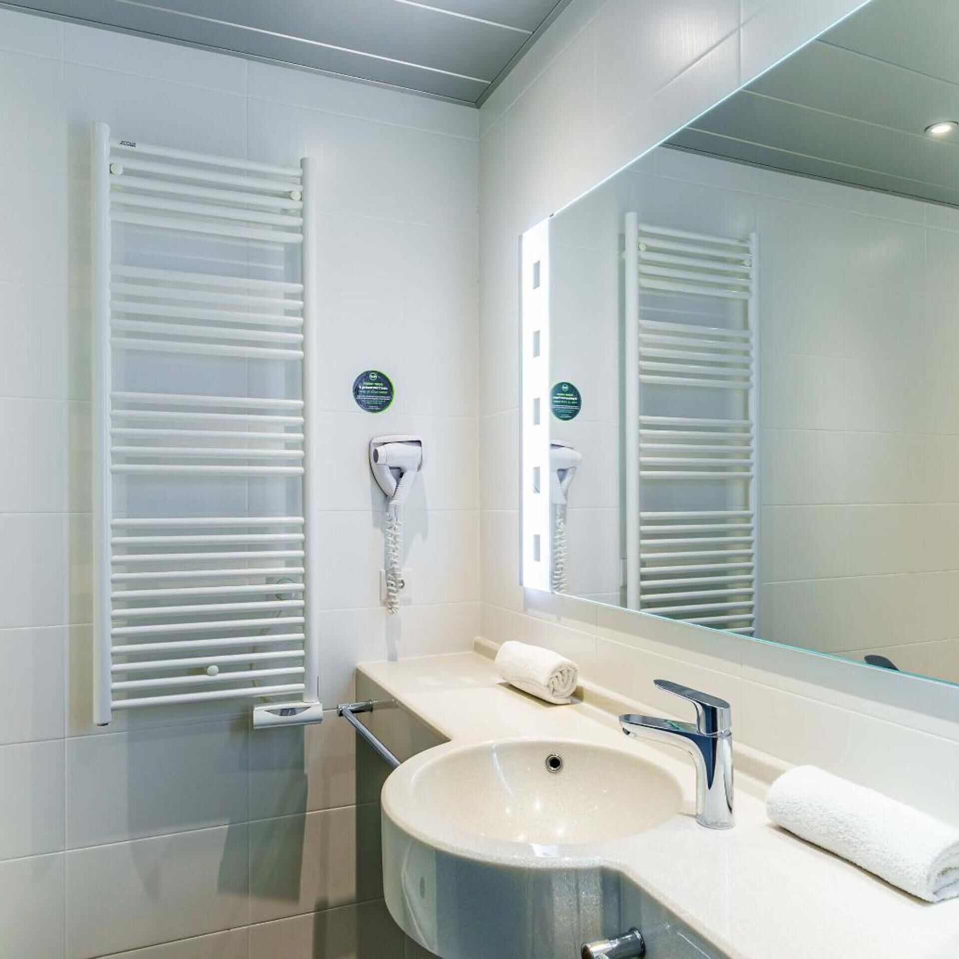 A modern bathroom with a sink, mirror, towel, and towel warmer.