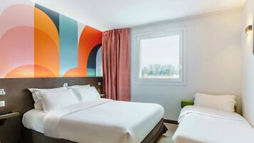 A hotel room with a large bed, a smaller bed, a window with a view, and a colorful abstract wall art.