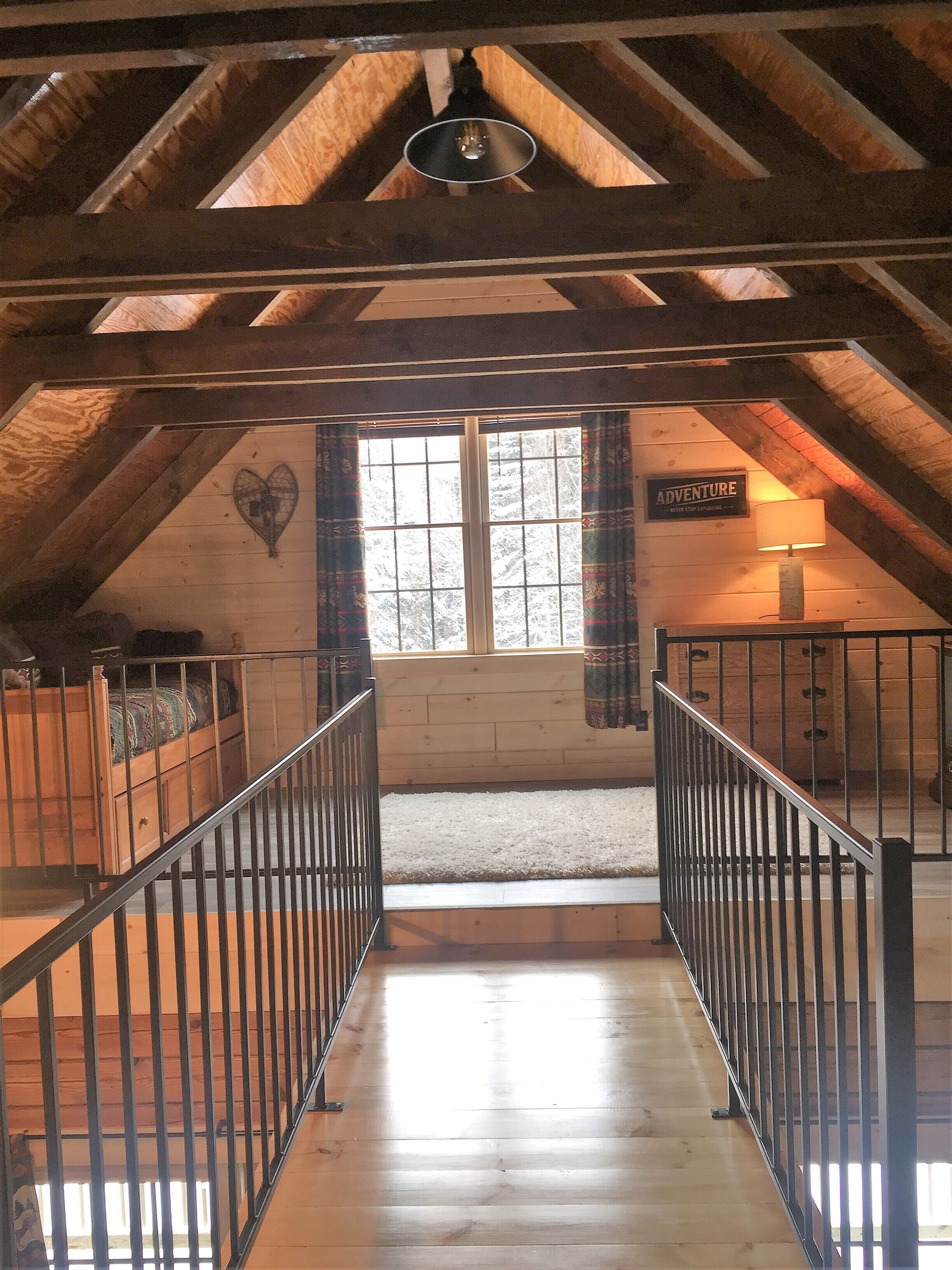 An attic room with a wooden floor, a window with curtains, a bed, a lamp, and a sign that says "ADVENTURE".