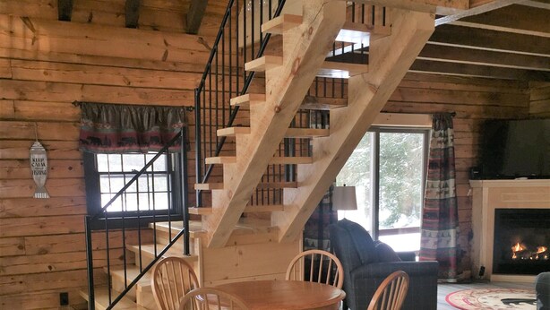 A wooden interior with a staircase, a fireplace, and a dining area with chairs and a table.