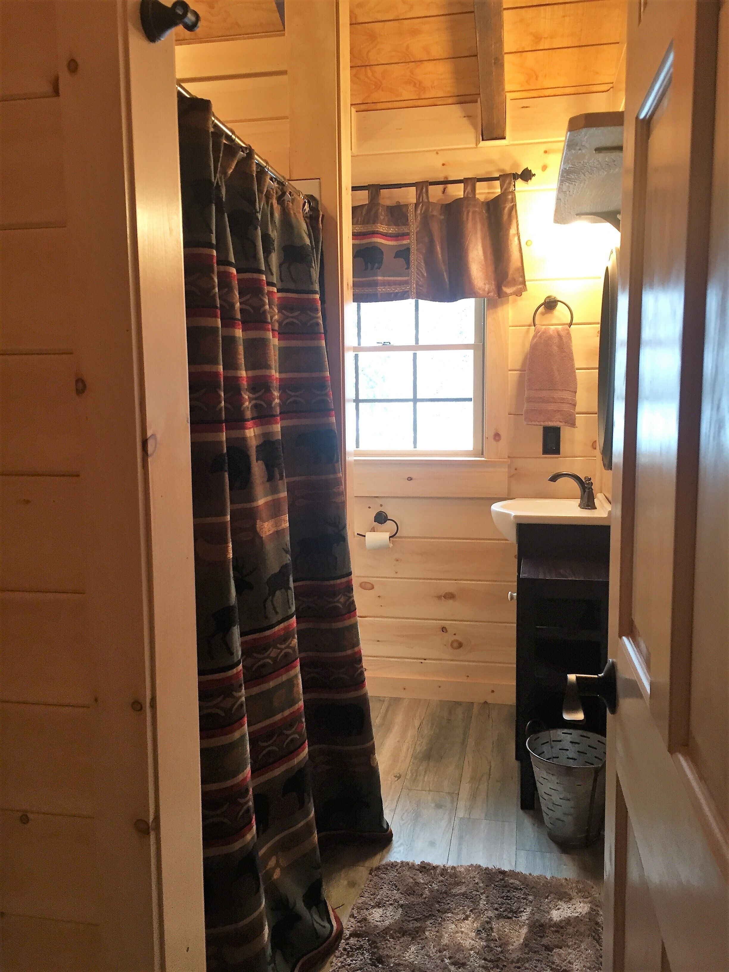 A wooden cabin bathroom with a window, sink, and towel rack.