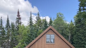 A wooden cabin with a porch, surrounded by a well-maintained lawn and flowering plants.