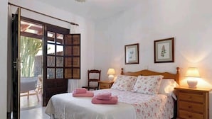 A bedroom with a bed, two bedside tables with lamps, a chair, and a door leading to an outdoor area. - Villa Las Palmeras in Playa Blanca (Playa Blanca)