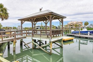 A wooden dock with a gazebo, a boat, and a marina with buildings in the background.