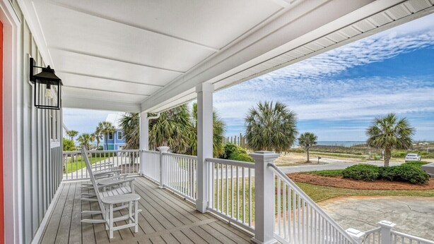 A covered porch with white railings, a wooden floor, and a view of the beach and ocean. - Glad Tidings - Six Bedroom, Four Bath Inlet-Front Beach Home (Garden City Beach)