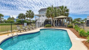 A swimming pool with lounge chairs, a covered seating area, and a house in the background. - Glad Tidings - Six Bedroom, Four Bath Inlet-Front Beach Home (Garden City Beach)