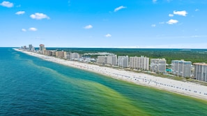 A coastal hotel with multiple high-rise buildings, a beachfront, and a clear blue sky.