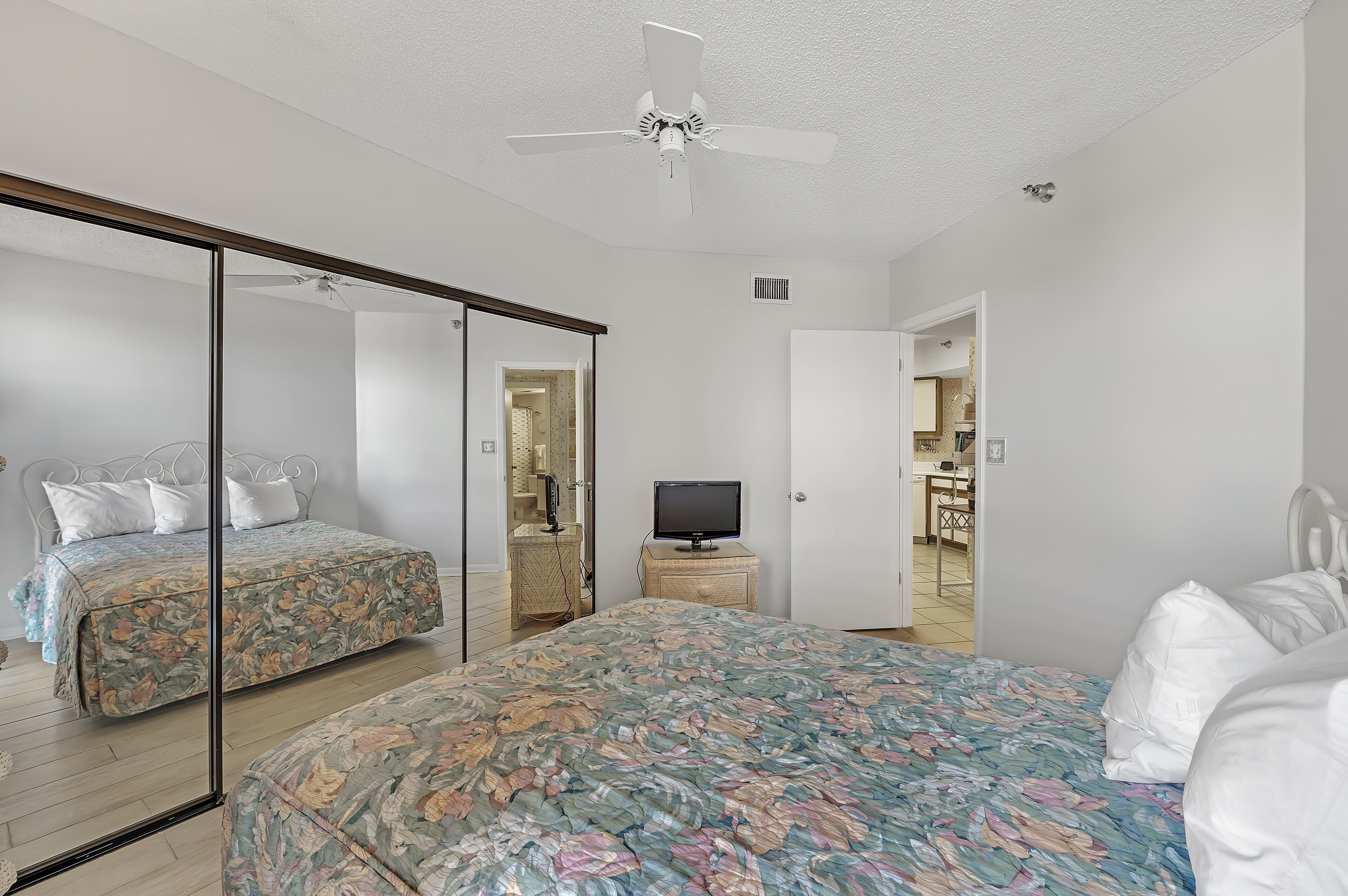 A bedroom with two beds, a television, and a ceiling fan.