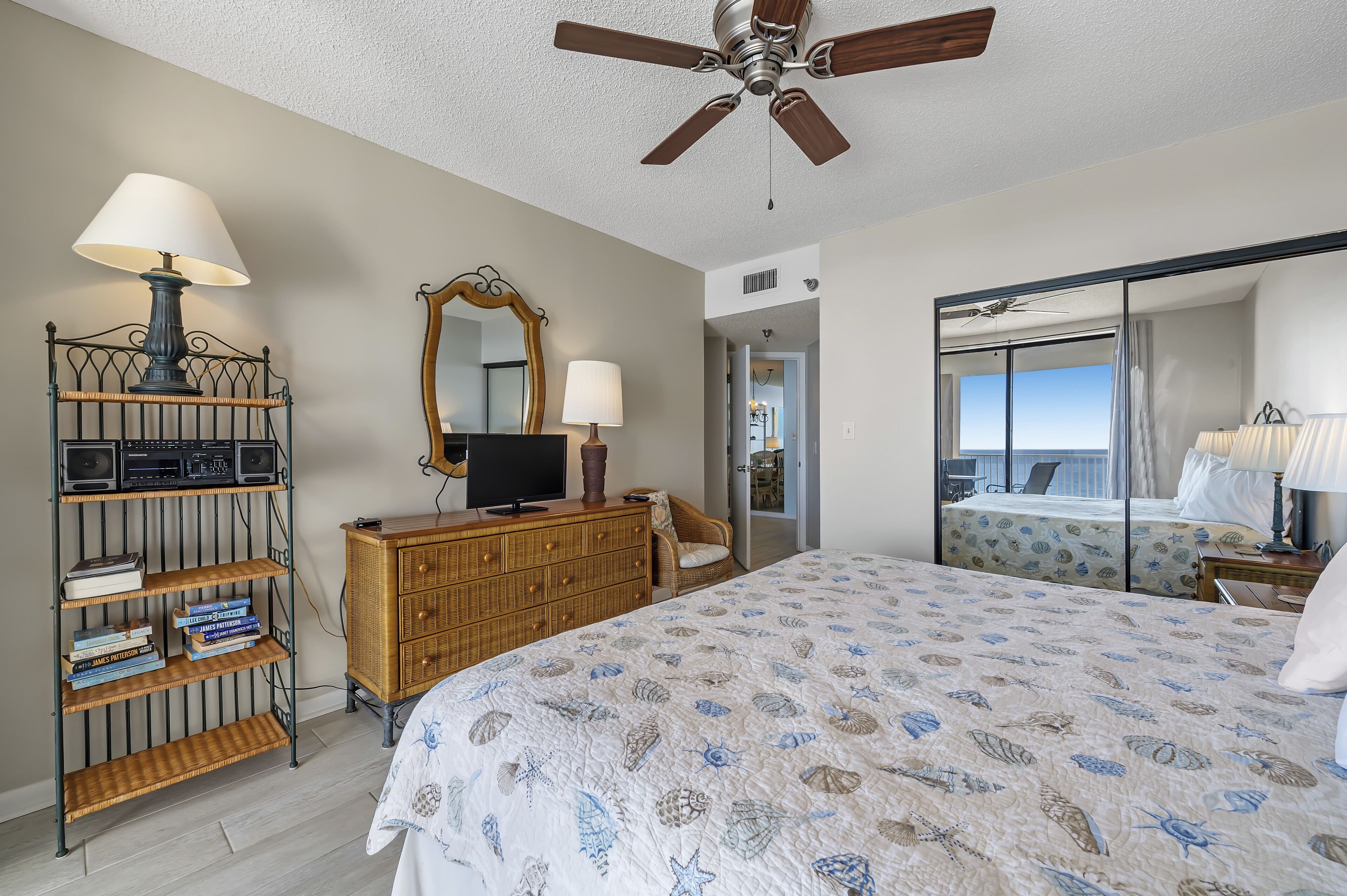 A bedroom with a bed, a dresser, a mirror, and a ceiling fan.
