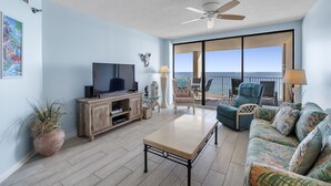 Een ruime woonkamer met een televisie, een salontafel, een bank en een balkon met uitzicht op de oceaan.
