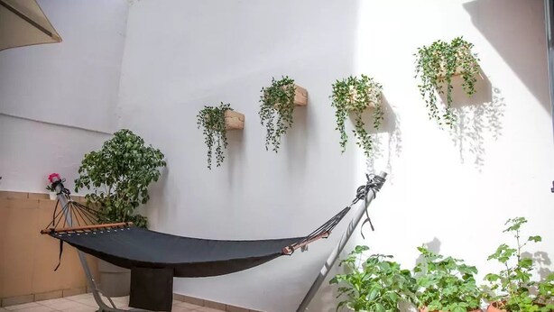 A hammock in a tiled area with potted plants and hanging planters against a white wall. - Thisio Modern House (Athens)