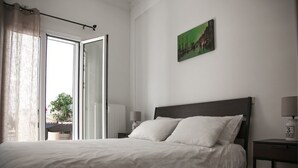 A bedroom with a bed, a nightstand, a lamp, a window with curtains, and a painting on the wall. - Thisio Modern House (Athens)