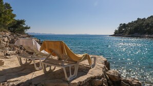 A beachside lounge with a table and two sun loungers, overlooking a calm sea and rocky coastline. - Secluded vacation home by the sea (Milna)