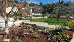 A garden with various plants and a building with a red roof in the background. - Secluded vacation home by the sea (Milna)