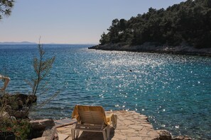 Una sedia vicino a una costa rocciosa, con vista libera sul mare e una collina boscosa sullo sfondo.