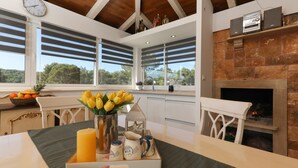 A modern kitchen with a stone fireplace, large windows, and a dining area with a table set for breakfast. - Secluded vacation home by the sea (Milna)