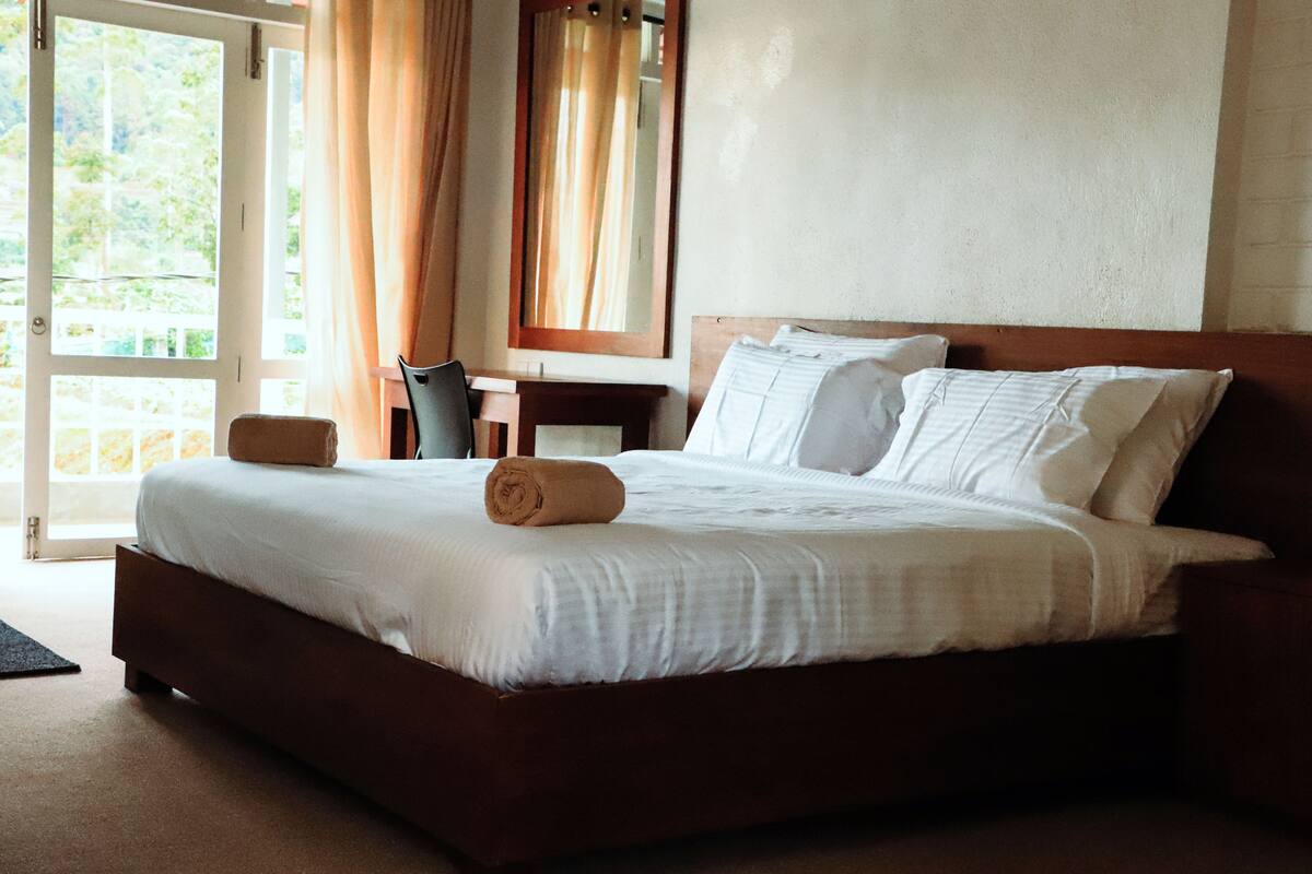 A neatly made bed with white linens and a brown headboard, a wooden nightstand, and a chair.