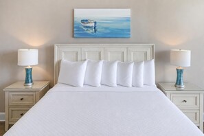 Habitación de hotel con una cama, ropa de cama blanca, cabecera, dos mesitas de noche con lámparas y un cuadro en la pared.