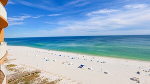 Ein Strand mit freiem Blick auf den Ozean, einem sandigen Ufer und einem Gebäude mit einem Balkon, der auf den Strand blickt.