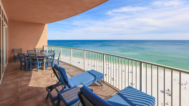 Ein Balkon mit Tisch und Stühlen, mit Blick auf einen Strand und einen klaren Blick auf das Meer.