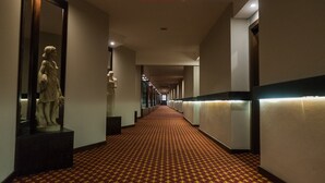 A hotel corridor with a patterned carpet, a statue on the left, and a long hallway with lights on the ceiling.