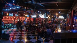 A crowded bar with checkered flooring and multiple screens displaying content.