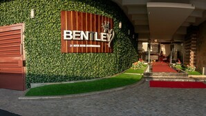 A hotel entrance with a "BENTLEY 24 HOUR ROOM ACCOMMODATION" sign, a red carpet, and a pathway leading to the entrance.