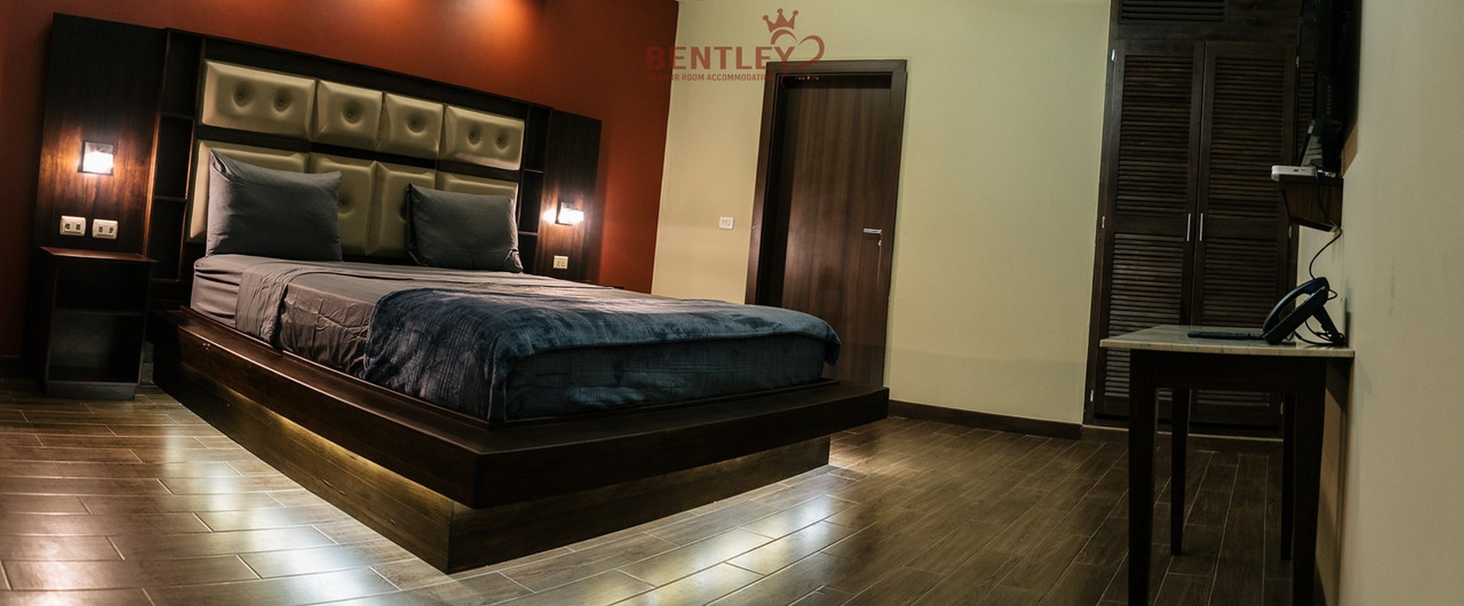 A modern bedroom with a large bed, a wooden headboard, a nightstand, and a desk with a chair.