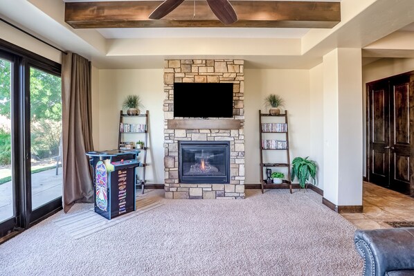 A living room with a stone fireplace, a flat-screen TV mounted above it, and a bookshelf with books and decorative items.