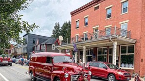 A vintage red fire truck parked on a street with buildings and a dog on the sidewalk.