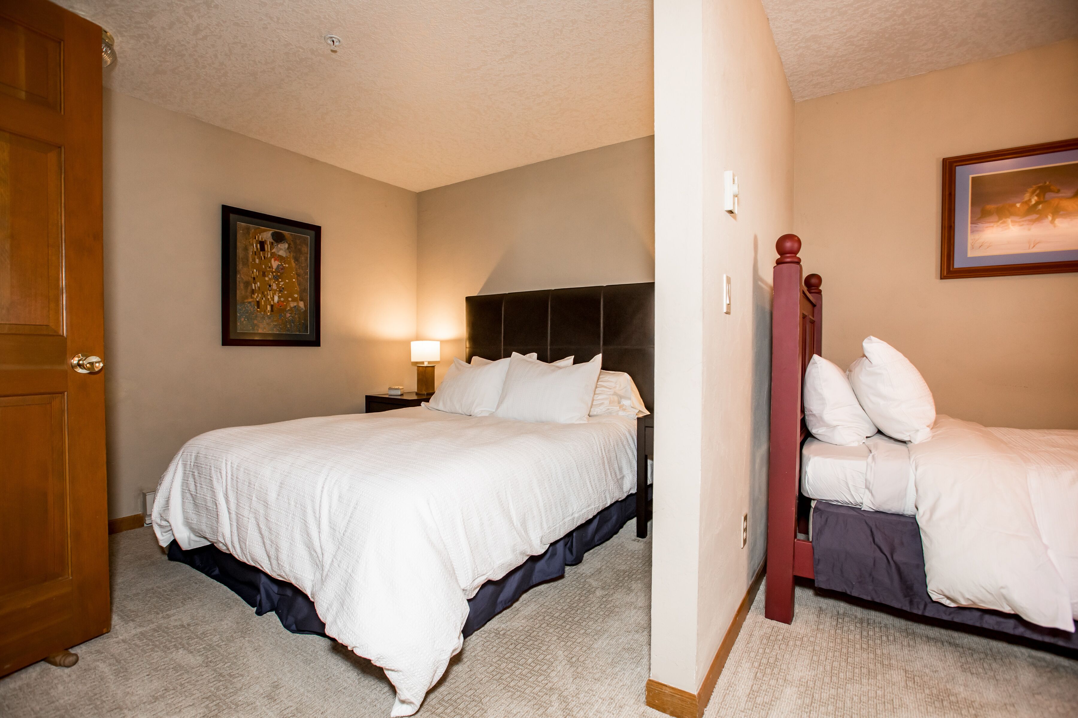 A bedroom with a large bed, a nightstand, a lamp, and a door.