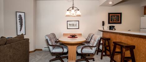 A compact living space with a round wooden dining table, two upholstered chairs, a bar area, and a kitchen counter.