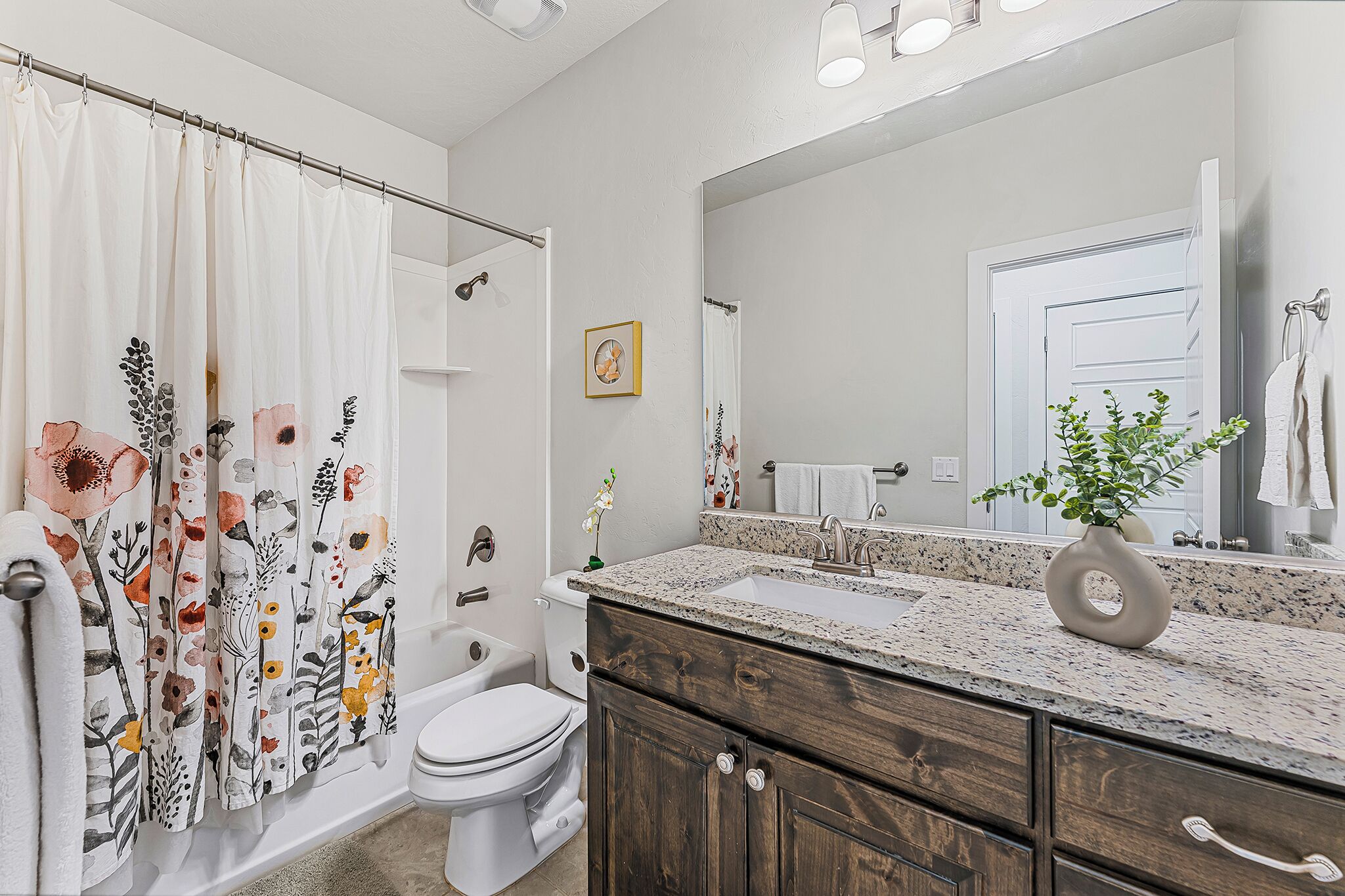 A bathroom with a shower curtain, toilet, sink, and vanity with a mirror.