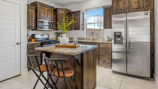 Una cocina con gabinetes de madera, electrodomésticos de acero inoxidable, encimera de granito y una zona de bar con taburetes.