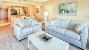 A living room with two light grey sofas, a white coffee table, and a kitchen in the background. - CRC 1111 - Beautiful Ground Floor Pool View Condo (St Augustine)