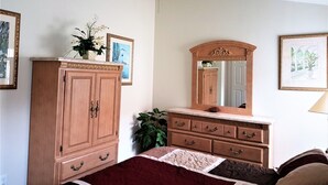A bedroom with a wooden wardrobe, a dresser, a bed with a red blanket, a ceiling fan, and framed pictures on the walls. - Executive Pool Home, 2 Master Suites, Lake View & Games Rm. WDW 3 Miles (Kissimmee)