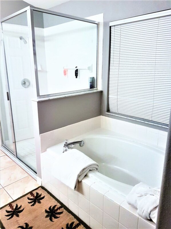 Une salle de bain moderne avec une douche à l’italienne en verre, une baignoire et une fenêtre équipée de stores.