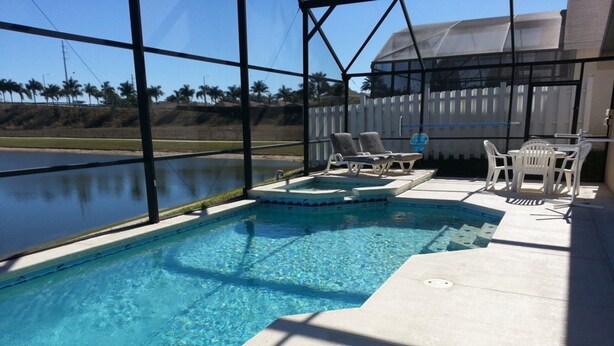 A swimming pool with clear blue water, surrounded by a deck with lounge chairs and a covered area. - Executive Pool Home, 2 Master Suites, Lake View & Games Rm. WDW 3 Miles (Kissimmee)