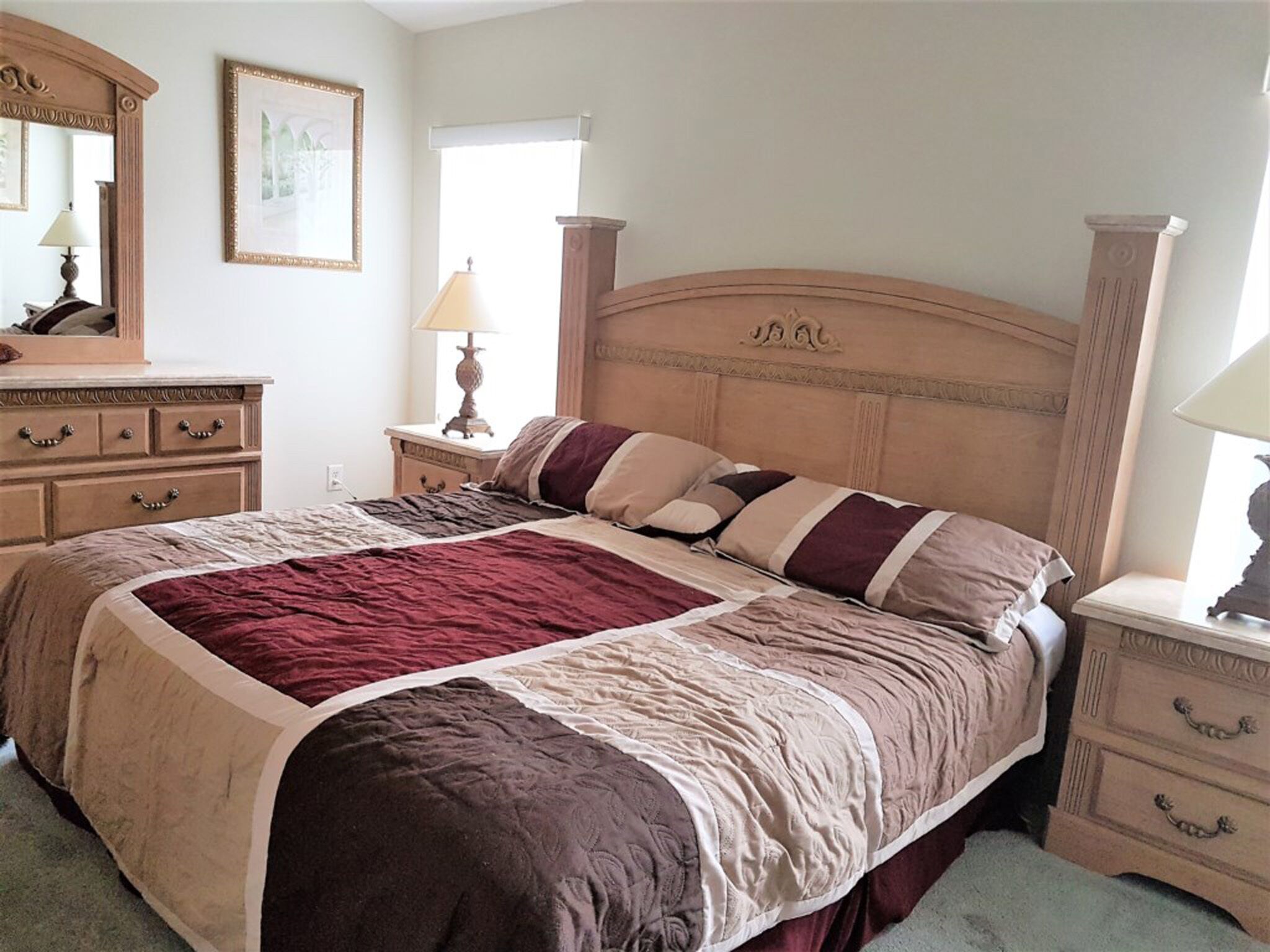 A bedroom with a large bed, wooden headboard, bedside tables, a dresser, a mirror, and a window with curtains.