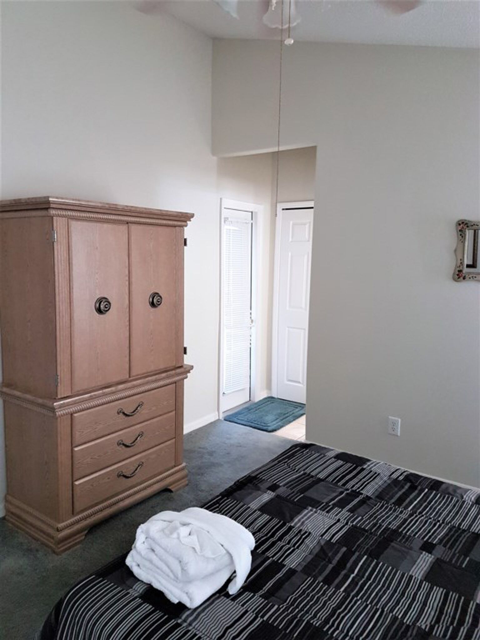 A bedroom with a bed, a wooden dresser, a door, and a small rug.